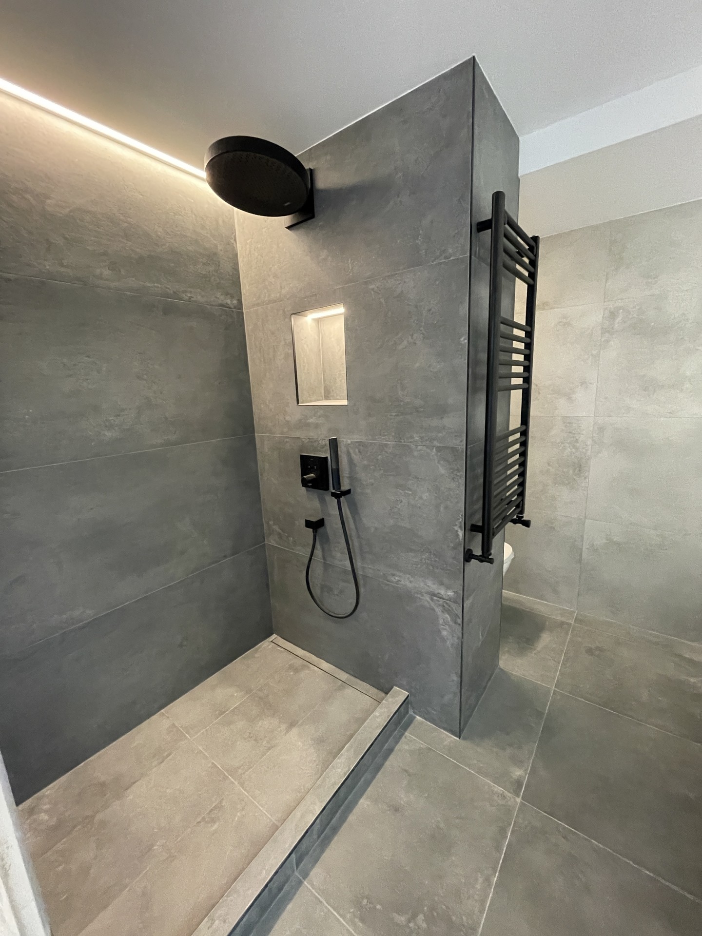 Ducha del baño principal con grifería negra y hornacina iluminada en Conde de Casal